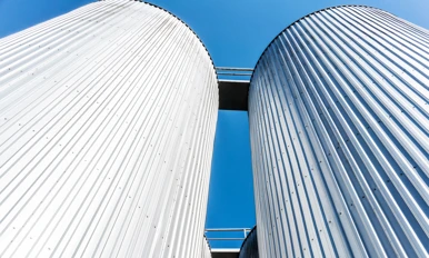 Two large, corrugated metal silos with a connecting walkway at the top, photographed from below