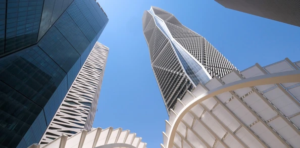 Modern skyscrapers with unique geometric designs against a clear blue sky, viewed from below.